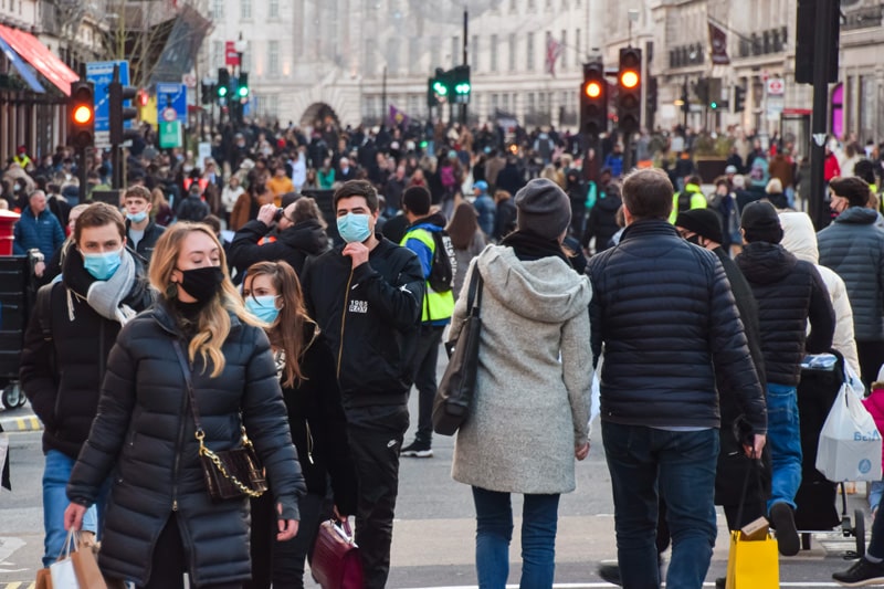 A busy high street full of shoppers carrying bags, with some people wearing face masks