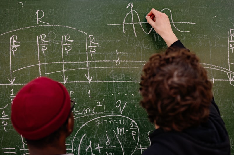 Two physics students writing formulas on a chalkboard