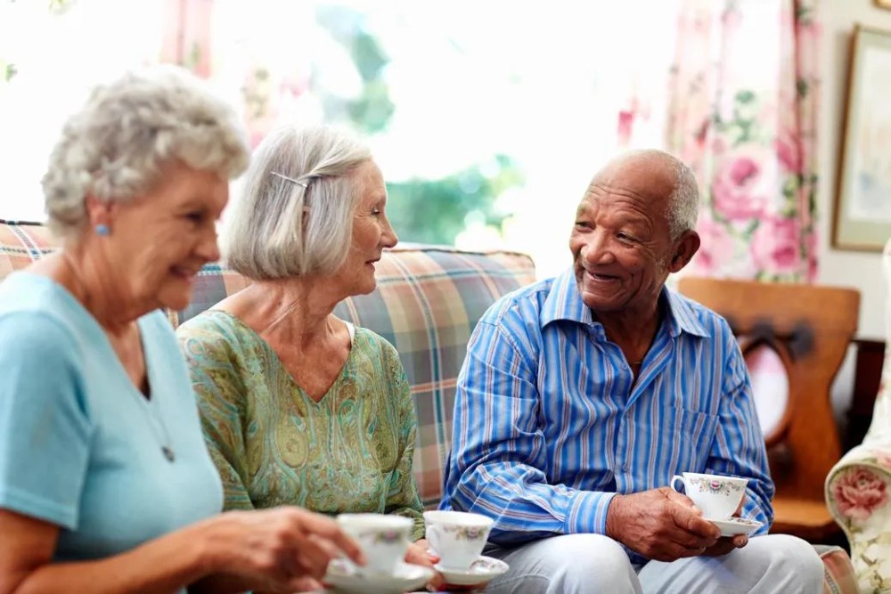 A group of older people chat on a sofa holding cups