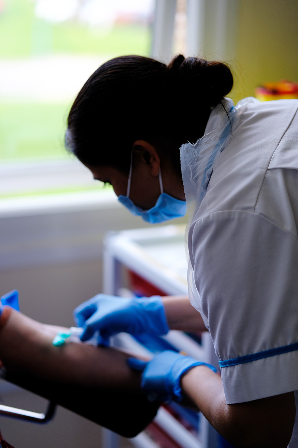 Rear view of a student nurse wearing white uniform, blue gloves and a face mask doing medical training.