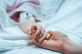 A hospital patient's hand, holding the hand of a loved one