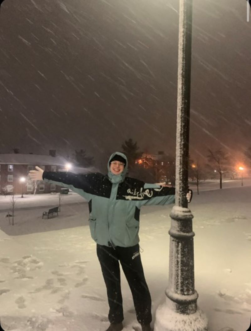 Person in snowy street posing by a street lamp post.
