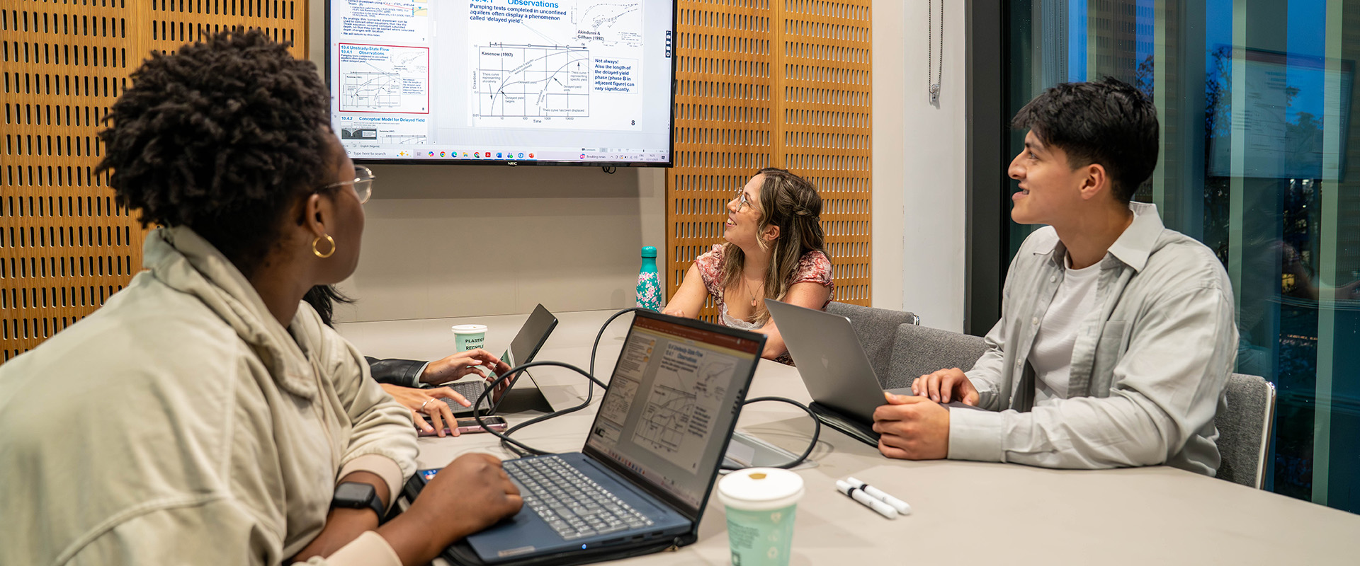 Three students around a table looking at a screen with a presentation
