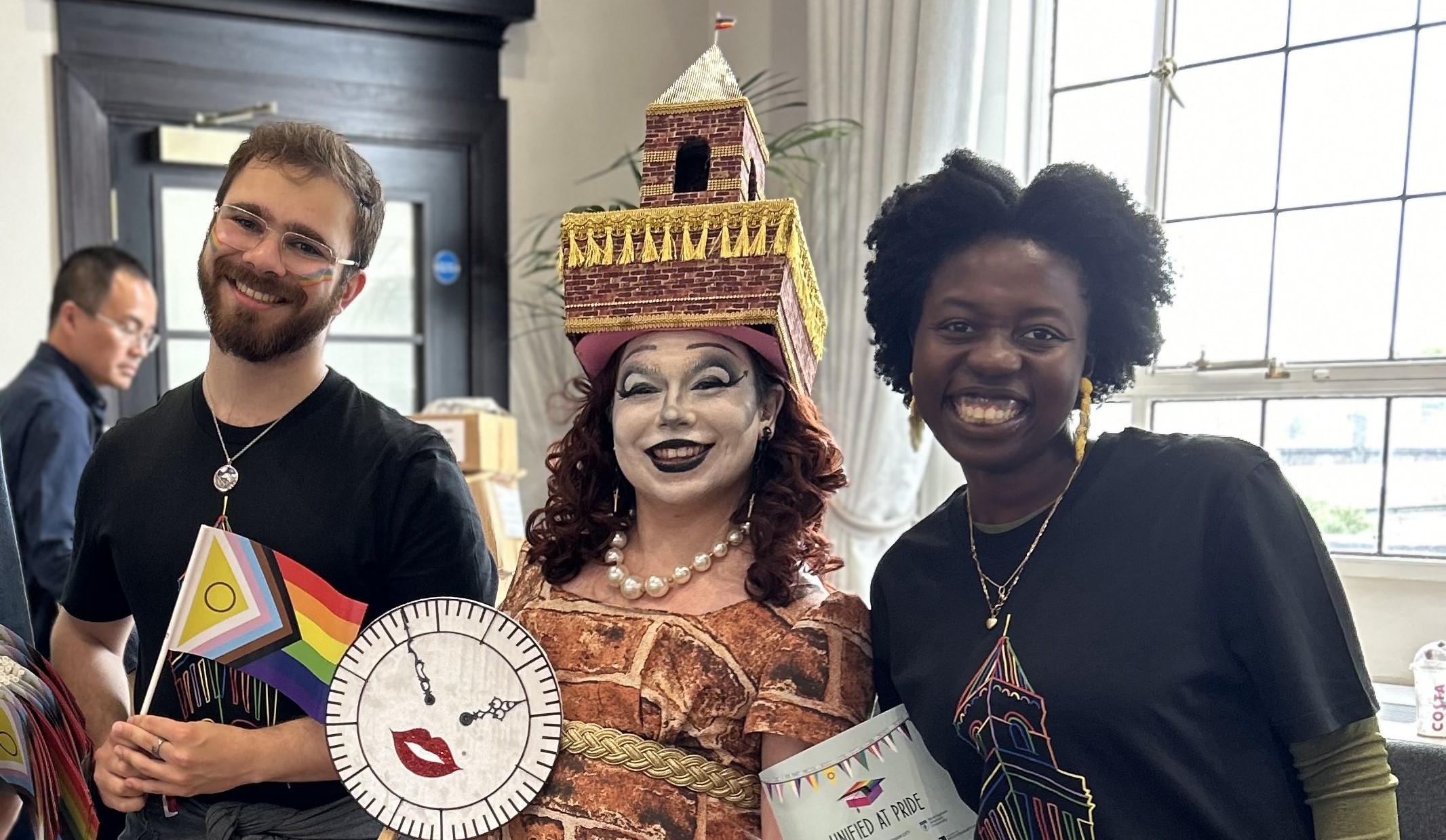 Three people stand together indoors wearing Pride-themed clothing. 