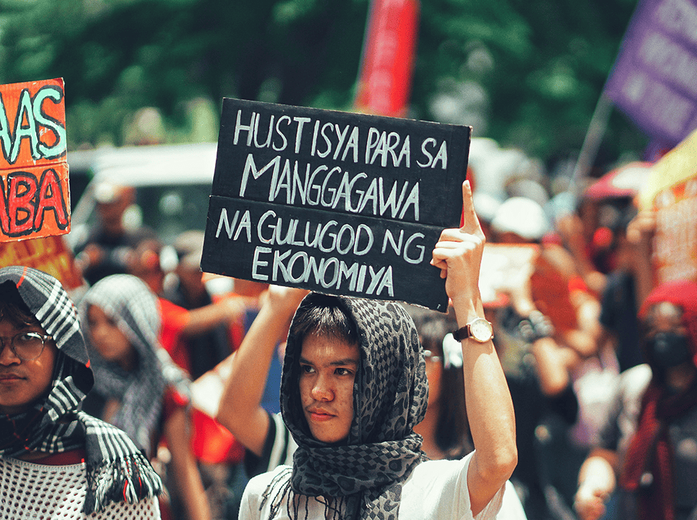 Young male Filipino protester holding a sign calling for justice for workers affected by the economy.