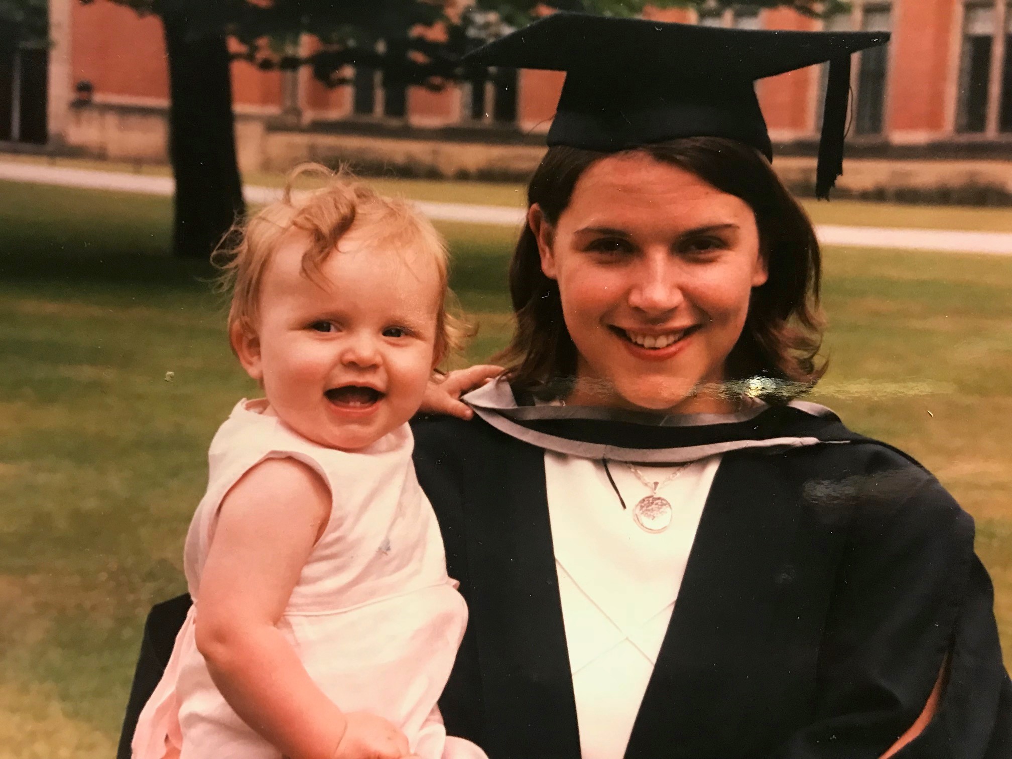 Woman in graduation gown and hat carrying a small child