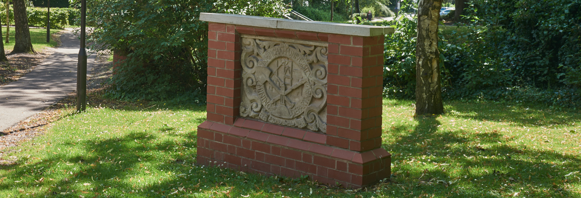 A stone plaque set into a small red brick wall against a green grassy landscape.
