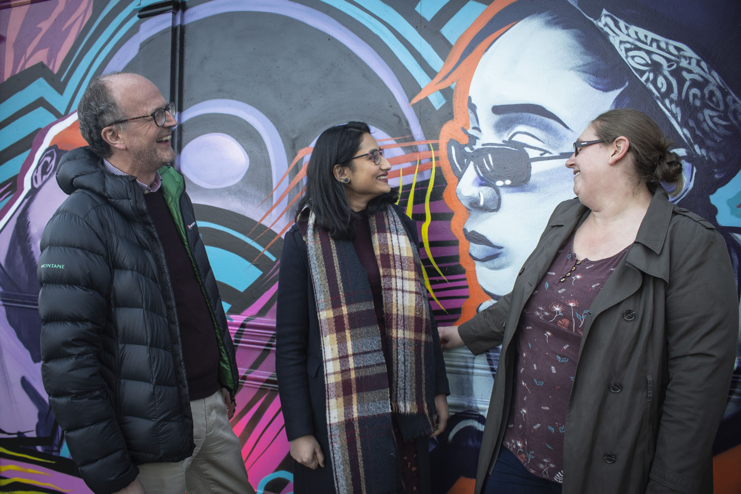 A group of three people stand in front of street art