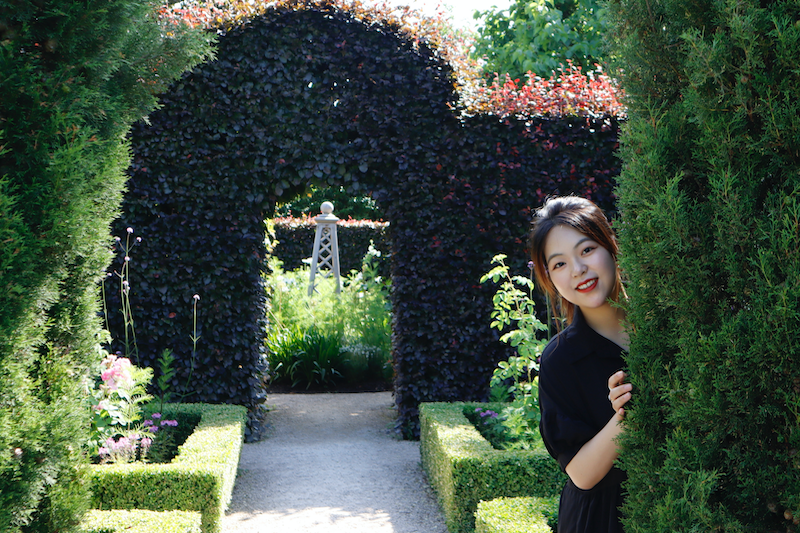 Sijia Jiang posing behind a hedge with a colourful leafy background