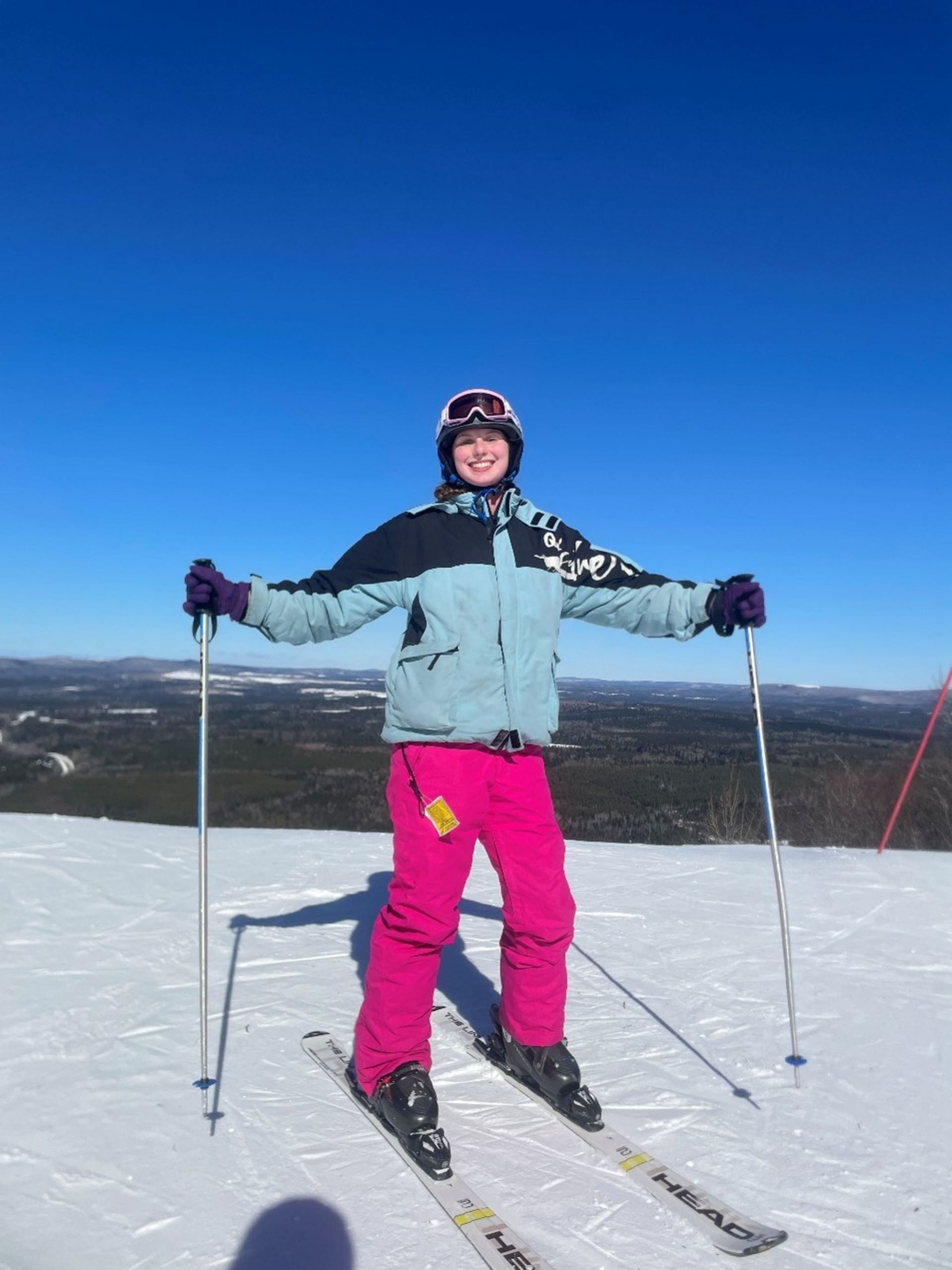 Skier smiling on top of snowy ski slope.