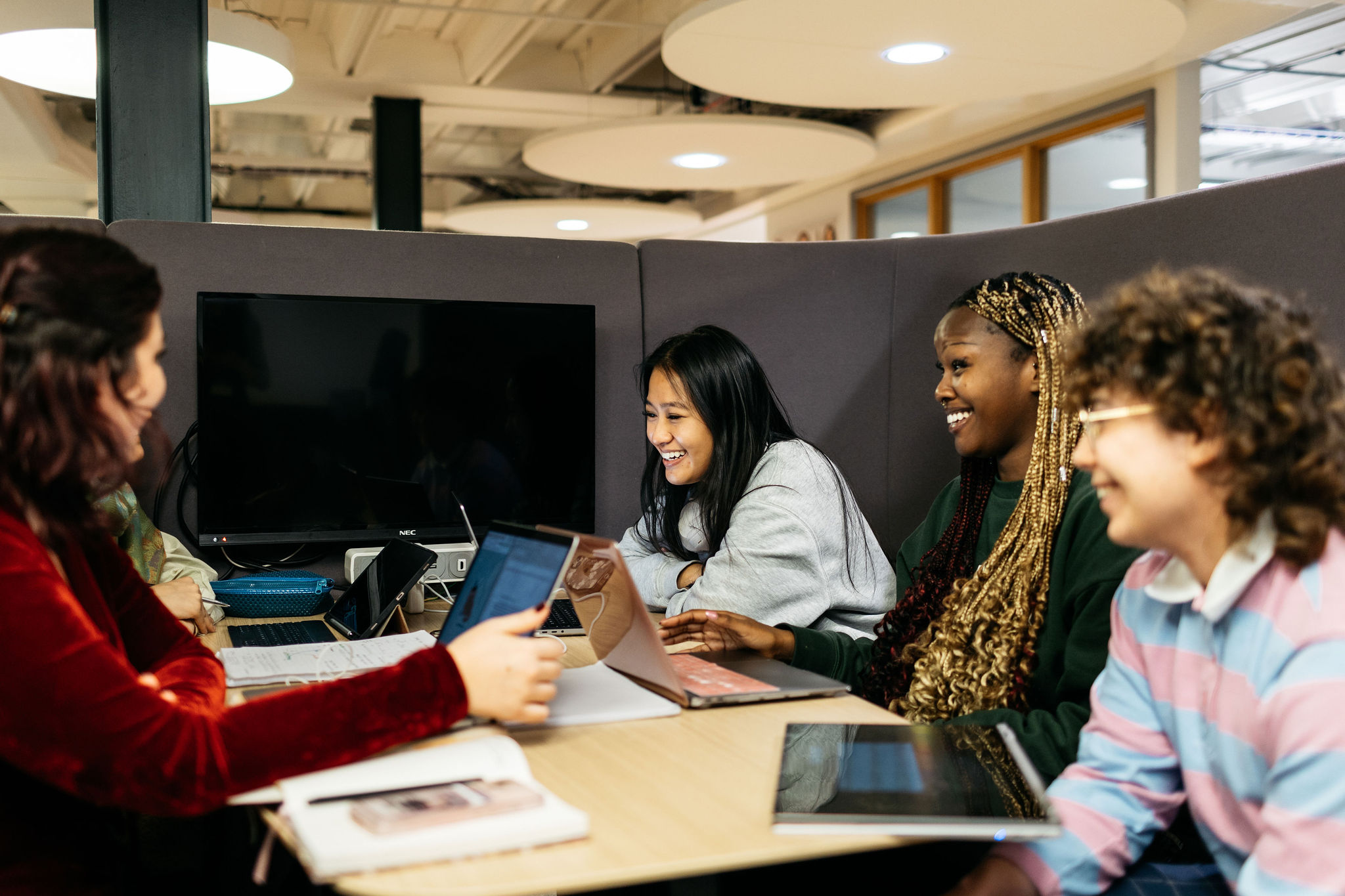 A group of students are sat with laptops in a study space talking with eachother