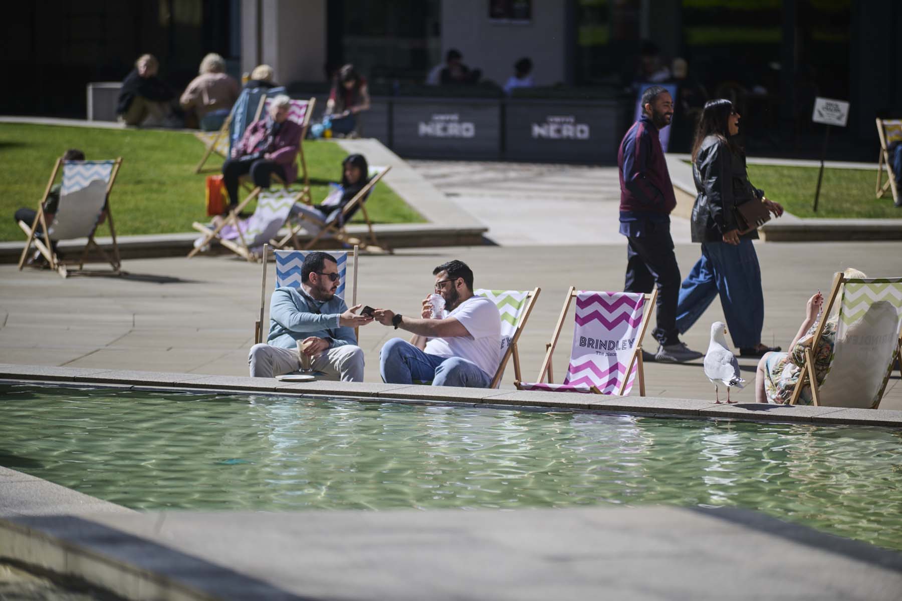 2 men sat on deck chairs next to water fountain