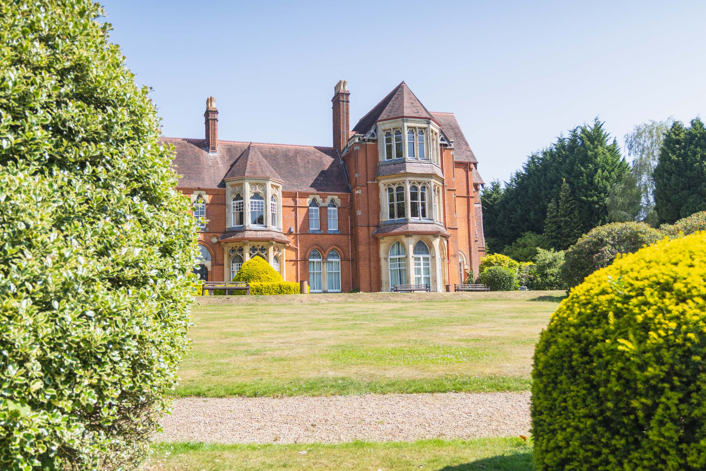 An image of Highbury Hall, an old manor house in green gardens, against blue skies. 