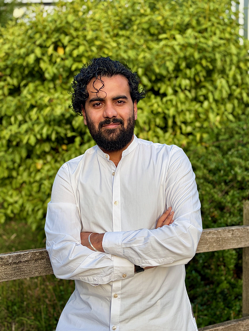 Dhawal, wearing a white shirt with his arms crossed, standing in front of a tree.