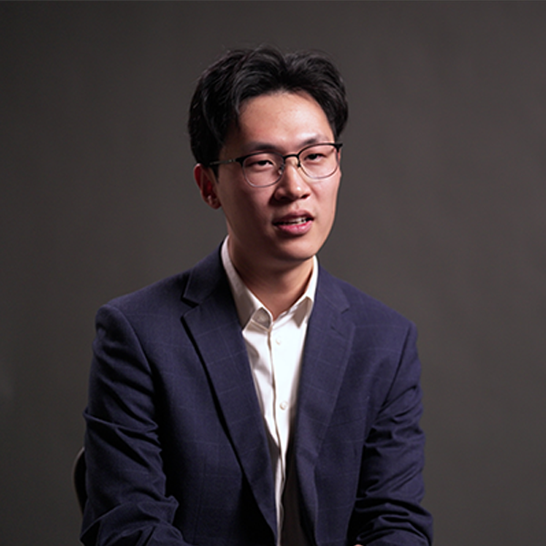 Dian Li wearing blue suit and white tie in front of grey background
