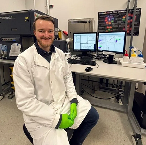 Dr Joseph Sturnam sitting in a lab wearing a white lab coat and smiling