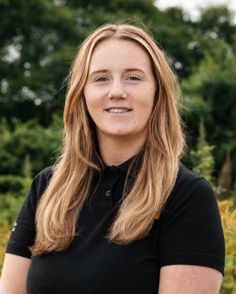 Portrait image of Kelly Bailey with long blonde hair wearing a black polo shirt