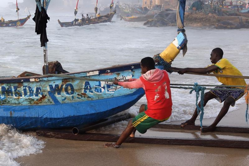 Two African men pulling a small boat onto a beach