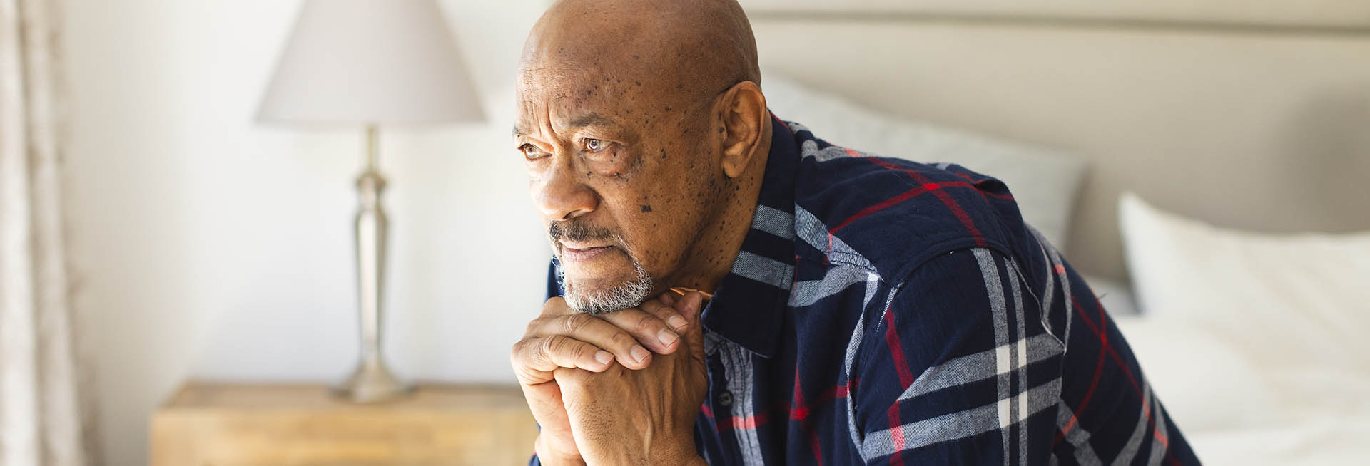 A middle aged man sits on a bed, looking thoughtful.