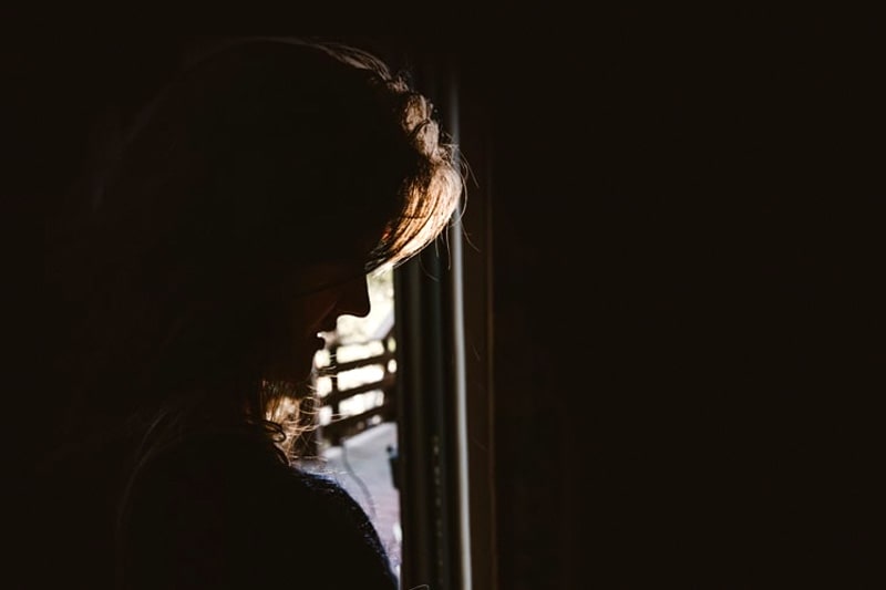 Silhouette of a sad woman with the light from a nearby window illuminating her profile