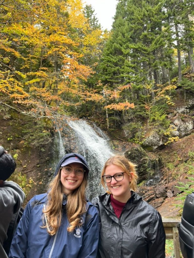 Two friends posing in front of a waterfall in hiking outfits.
