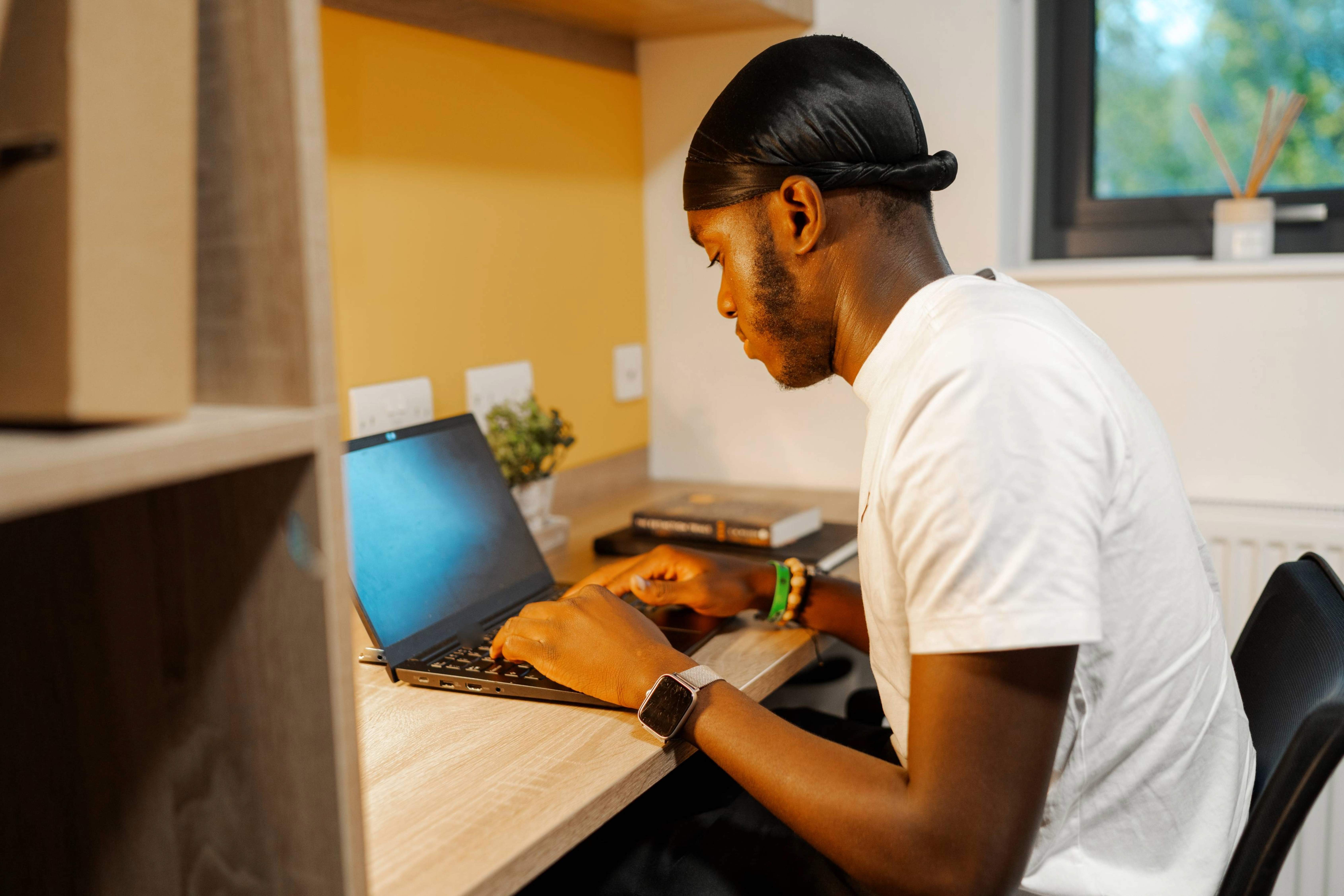 A student sitting at his desk typing on his laptop