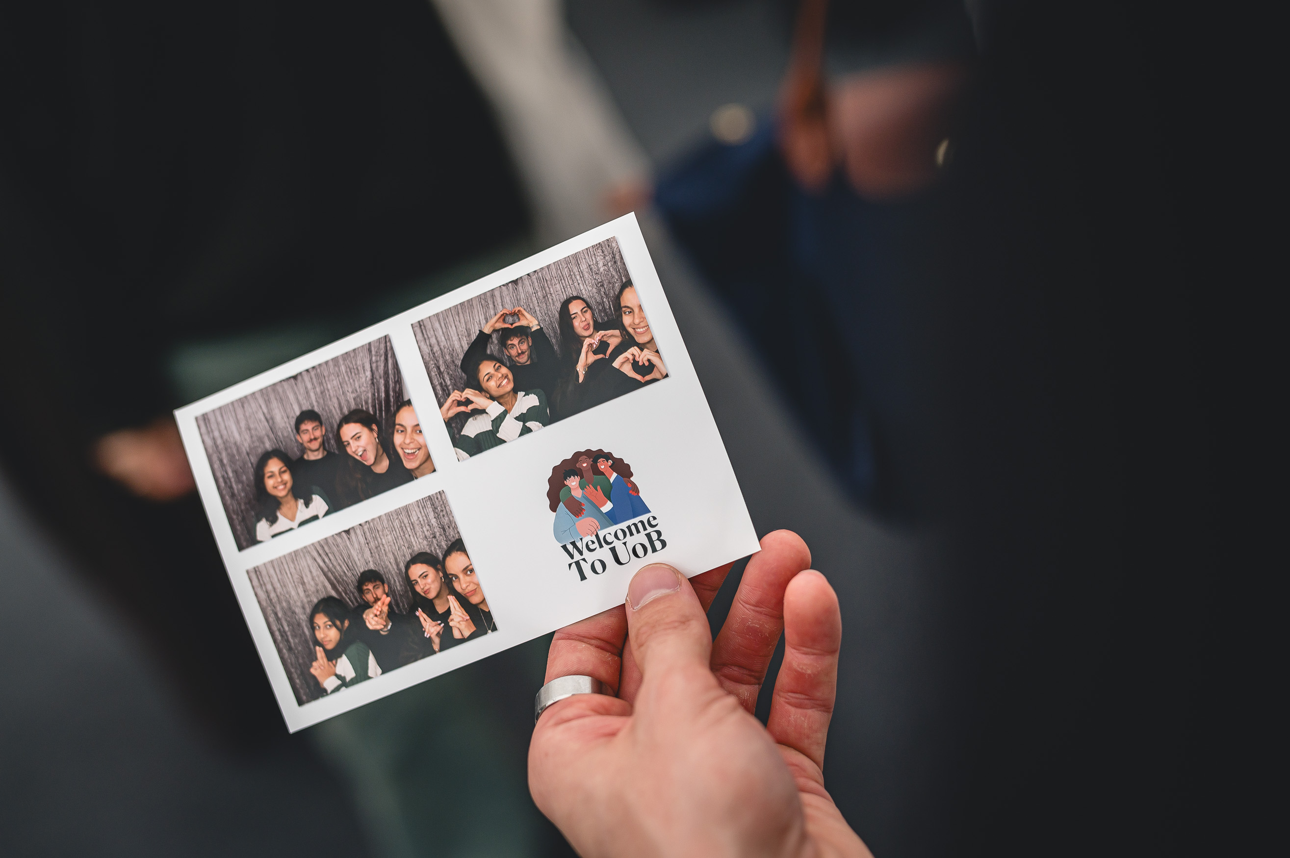 A hand holds a photobooth printout with three photos of students posing together