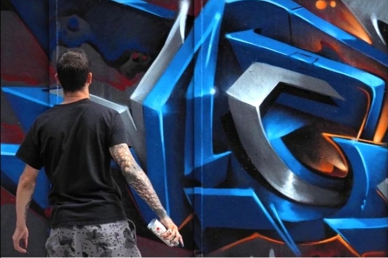 Man with spray paint in front of mural