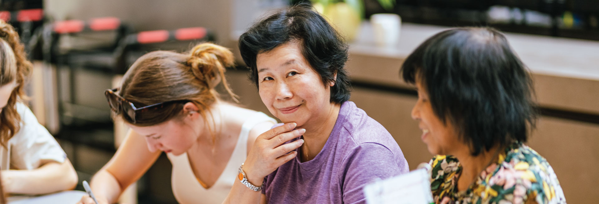 Three women sit at a table, one looks at the camera smiling.
