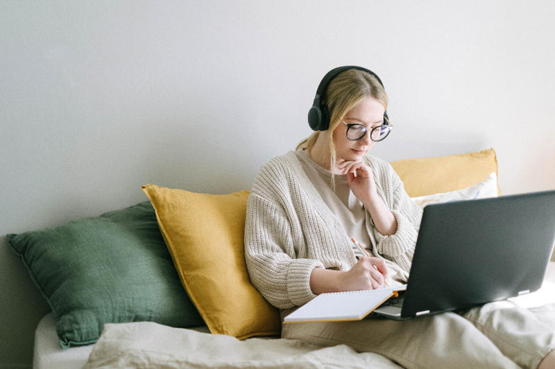 Blond woman in glasses sits on sofa with laptop