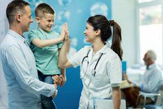 Young boy held by dad giving high five to nurse